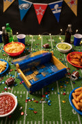 Game day setup with snacks, drinks, and a toy cash register on a grass-like surface with sports-themed decorations.